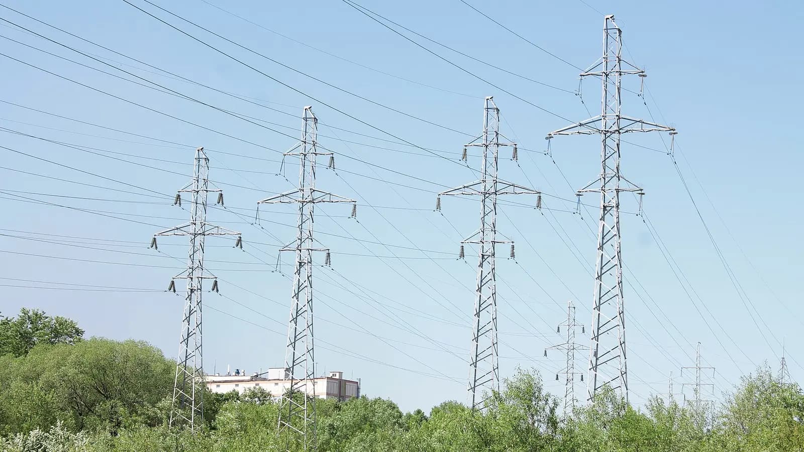 A high-voltage transmission tower silhouetted against a dark server hall with glowing racks
