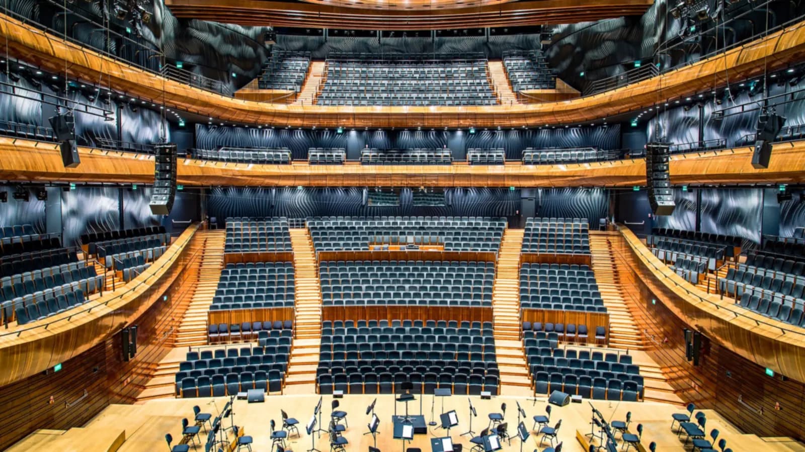 A stage spotlight on an empty podium facing rows of dark seats, with red light spilling from behind a curtain
