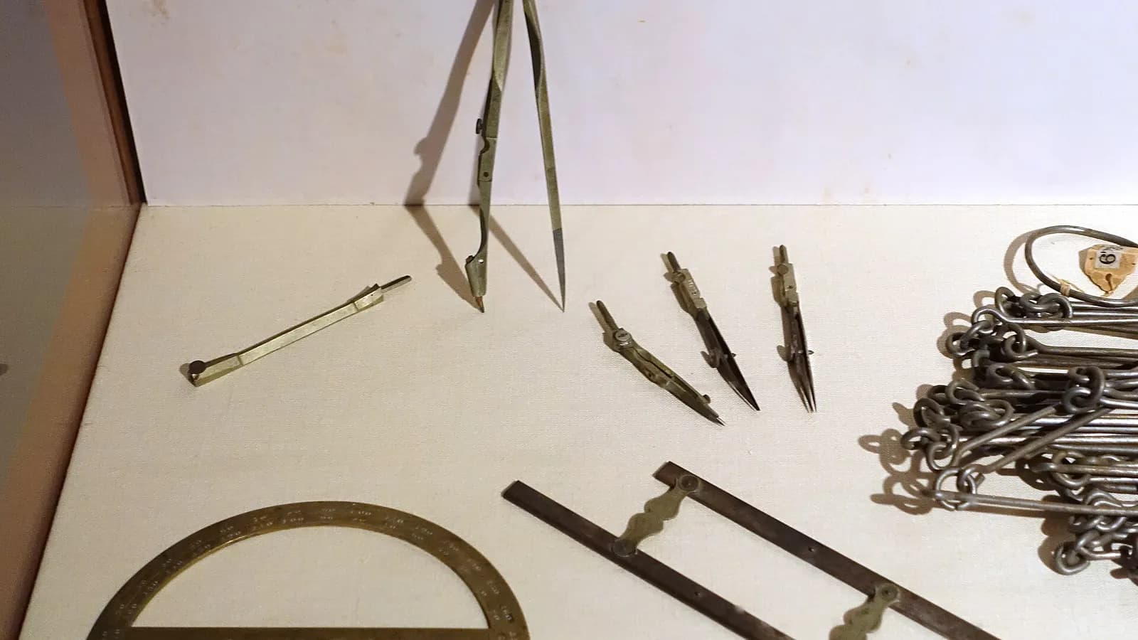 Antique brass and steel drafting tools, including dividers, a protractor and a parallel ruler, laid out on a pale surface