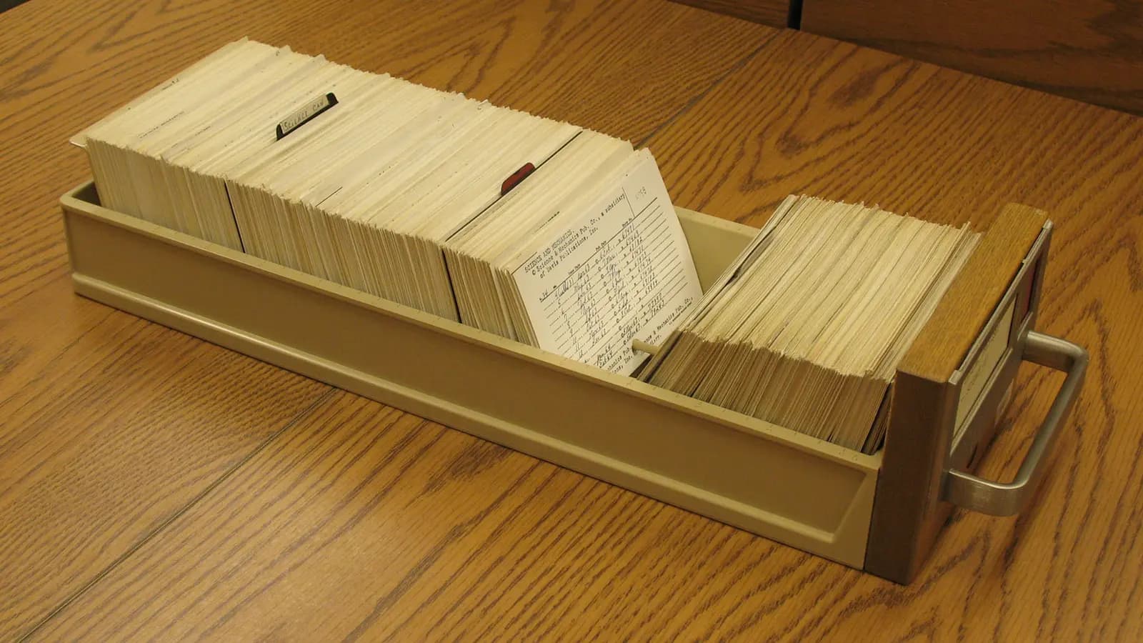 A librarian's index card cabinet feeding a single glowing card into a lit page